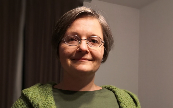 Kobieta z krótkimi włosami w zielonym swetrze, uśmiechająca się do kamery.