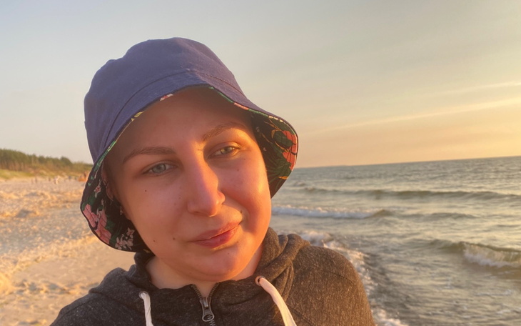 Osoba na plaży o zachodzie słońca, przytulnie uśmiechnięta, w kapeluszu.