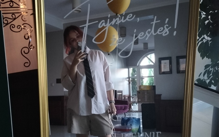 Osoba w lustrze, z balonami i napisem 'Fajnie, że jesteś!'