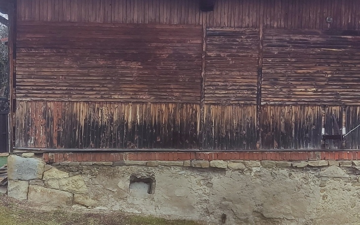Zniszczona drewniana ściana budynku, z widocznymi śladami pożaru.