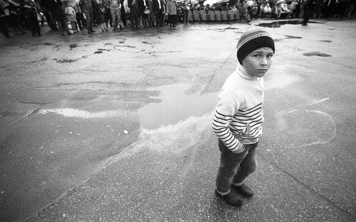 Chłopiec w swetrze, stojący na ulicy, z zamyśloną miną.