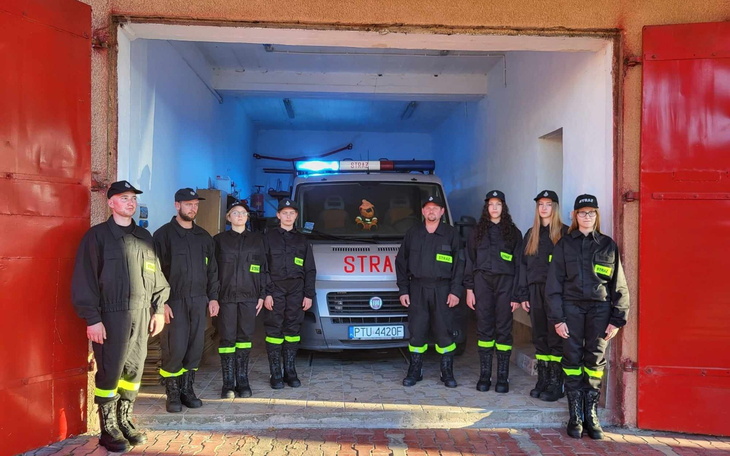 Grupa strażaków w mundurach przed wozem strażackim.