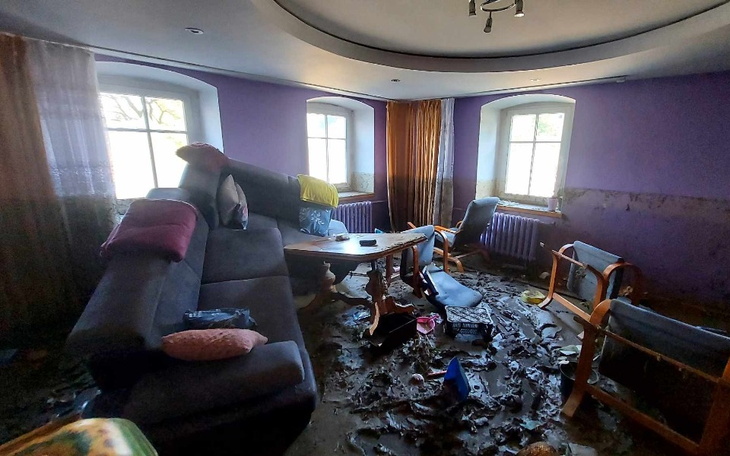 Zniszczony pokój z meblami w nieładzie i zniszczeniami po zalaniu.