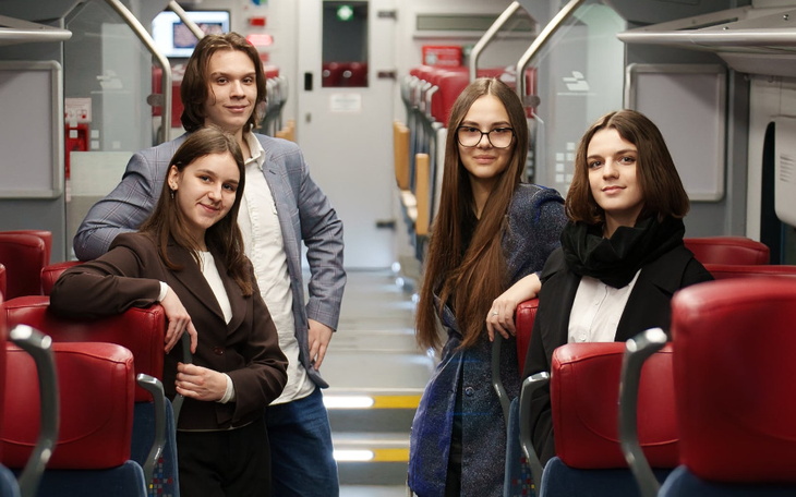 Czwórka młodych ludzi pozujących w nowoczesnym wnętrzu pociągu.