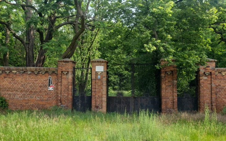 Zamknięta brama w parku, otoczona zielenią i drzewami.
