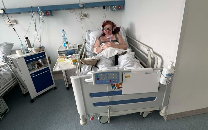 Kobieta w łóżku szpitalnym, korzystająca z telefonu, w słuchawkach.