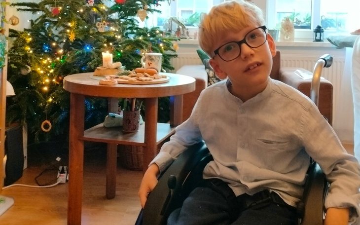 Chłopiec na wózku inwalidzkim, siedzący przy stole z jedzeniem.