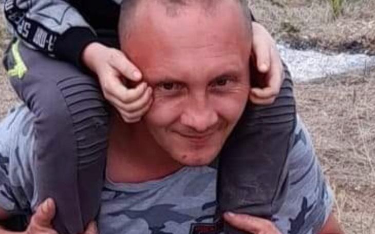 Mężczyzna z dzieckiem na plecach, uśmiechnięty.