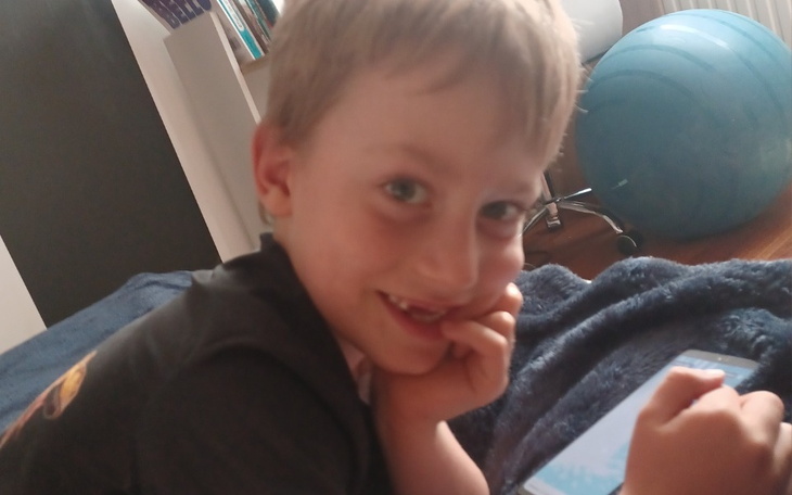 Chłopiec uśmiechający się, leżący na kanapie z telefonem.