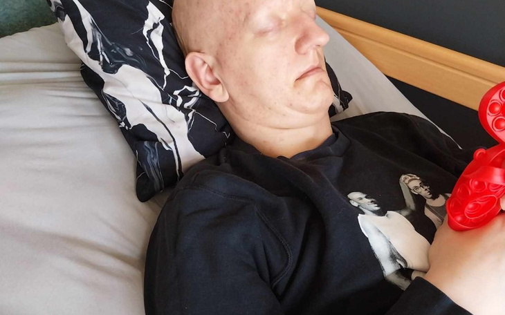 Chłopak odpoczywa w łóżku, trzymając w rękach czerwoną zabawkę.