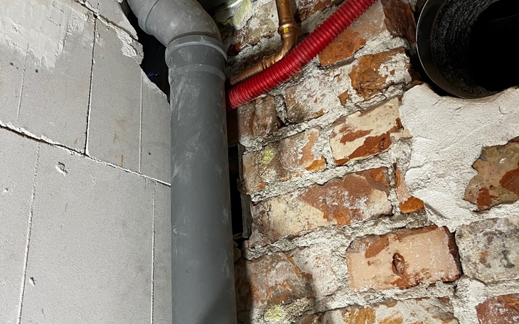 Fragment ściany z cegły, rura i instalacje w piwnicy.