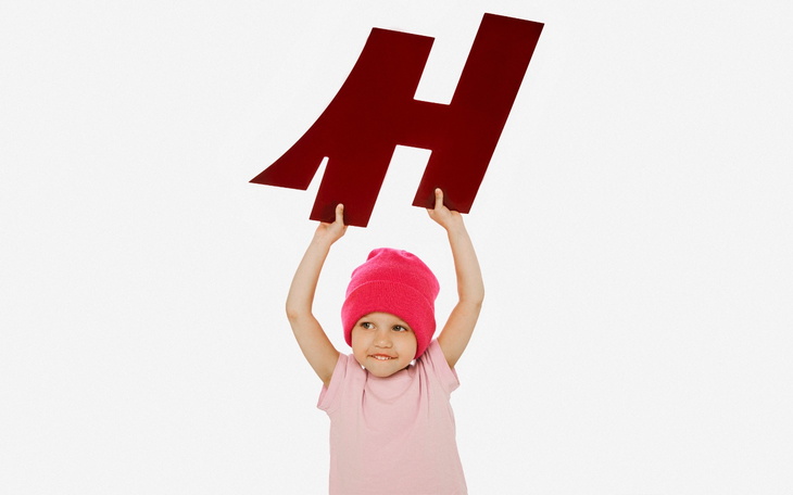 Dziecko w różowej czapce trzyma dużą literę H.