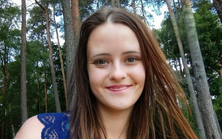Młoda kobieta na zewnątrz z ciemnymi włosami, w tle drzewa