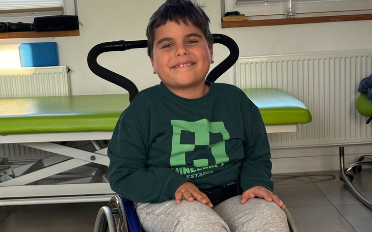 Chłopiec na wózku inwalidzkim uśmiechający się do kamery.