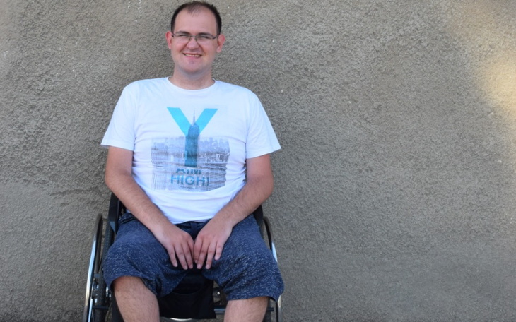 Mężczyzna na wózku inwalidzkim, uśmiechający się do kamery.