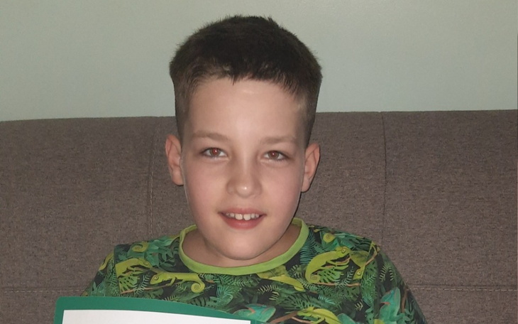 Chłopiec w zielonej koszulce, trzymający kartkę z uśmiechem.