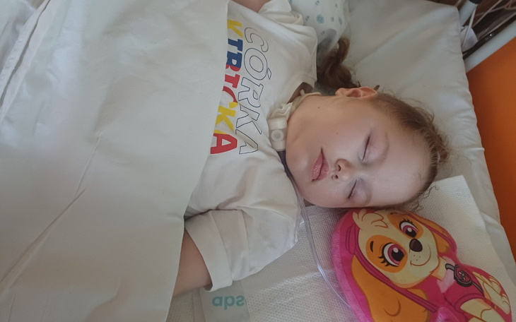 Mała dziewczynka śpiąca w szpitalnym łóżku, z uśmiechem na twarzy.