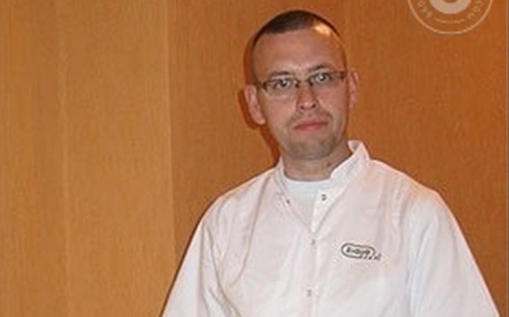 Mężczyzna w białym fartuchu, patrzy w obiektyw.