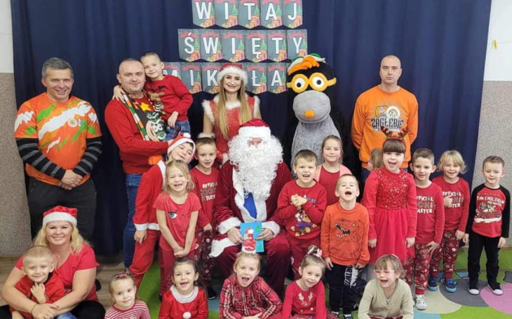 Grupa dzieci i dorosłych w strojach świątecznych z Mikołajem.