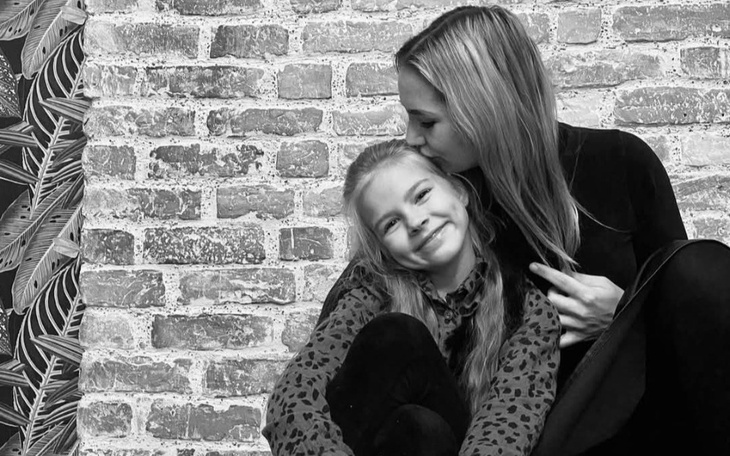 Kobieta całująca dziewczynkę w czoło, obie uśmiechnięte.