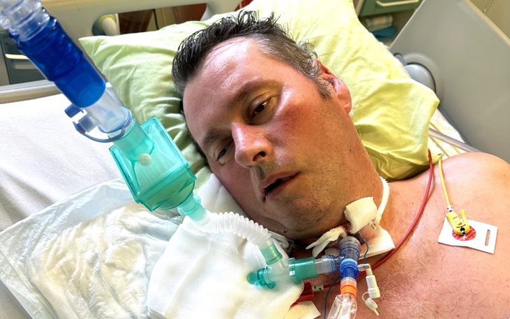 Mężczyzna w szpitalu z rurkami medycznymi, leżący na łóżku szpitalnym.