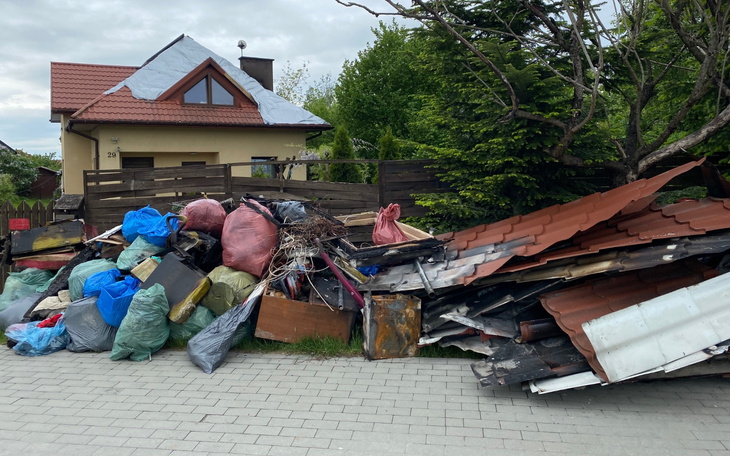 Wielka sterta odpadów i śmieci przed domem, w otoczeniu zieleni.