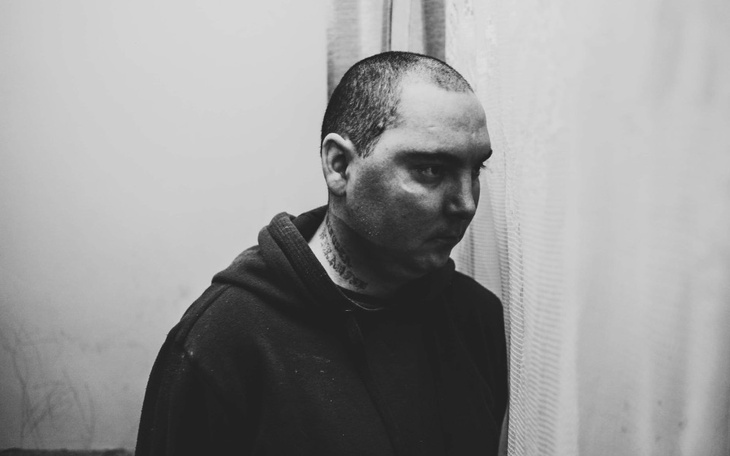 Mężczyzna w ciemnym ubraniu, patrzący w dół.