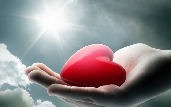 Ręka trzymająca czerwone serce na tle nieba.
