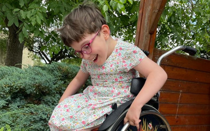 Uśmiechnięta dziewczynka w wózku inwalidzkim na świeżym powietrzu.