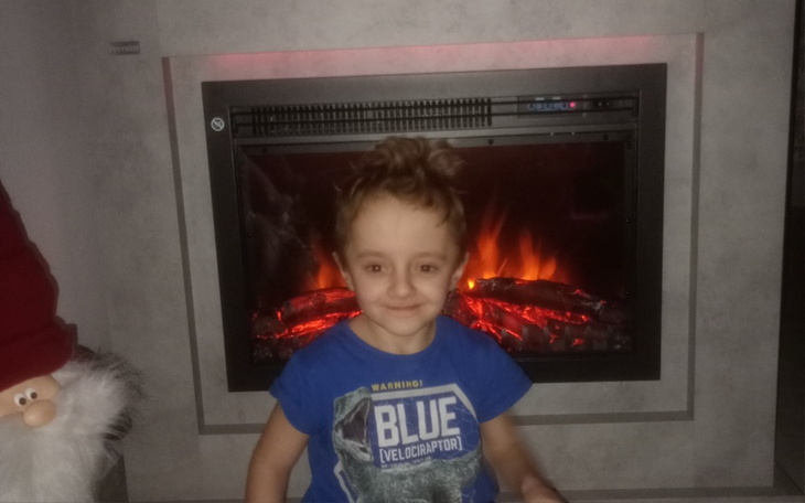 Chłopiec uśmiechający się przed kominkiem, w ciepłym otoczeniu.