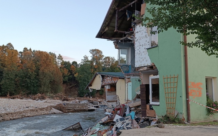 Zniszczony budynek nad rzeką, z widocznymi uszkodzeniami.