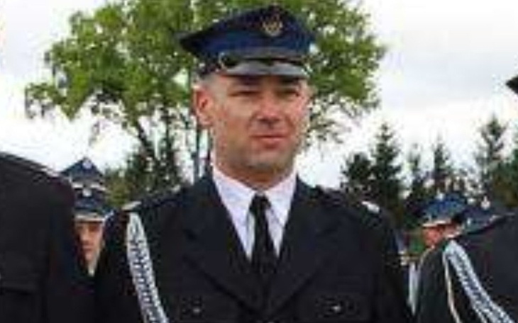 Mężczyzna w mundurze policyjnym, na tle zieleni.