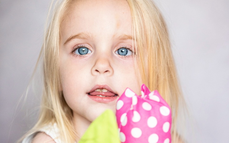 Mała dziewczynka z niebieskimi oczami trzyma kolorowe balony.