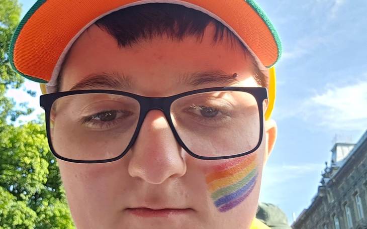 Młody człowiek z tęczowym malunkiem na policzku.