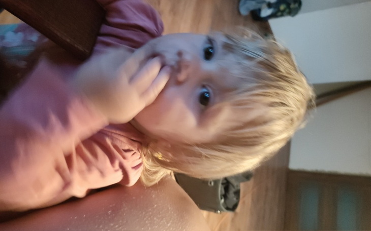 Małe dziecko z blond włosami, trzymające palec w buzi.