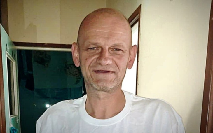 Mężczyzna w białej koszulce uśmiechający się w drzwiach.