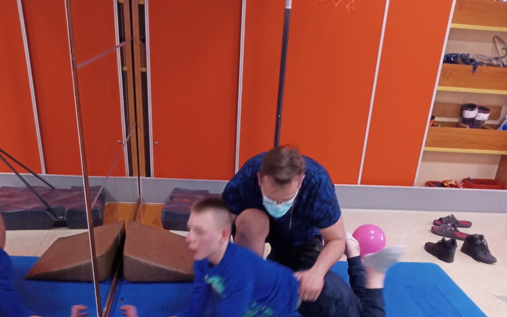 Mężczyzna pomagający dziecku w aktywności fizycznej w sali.