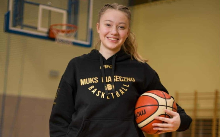 Młoda koszykarka trzymająca piłkę, uśmiecha się do kamery.