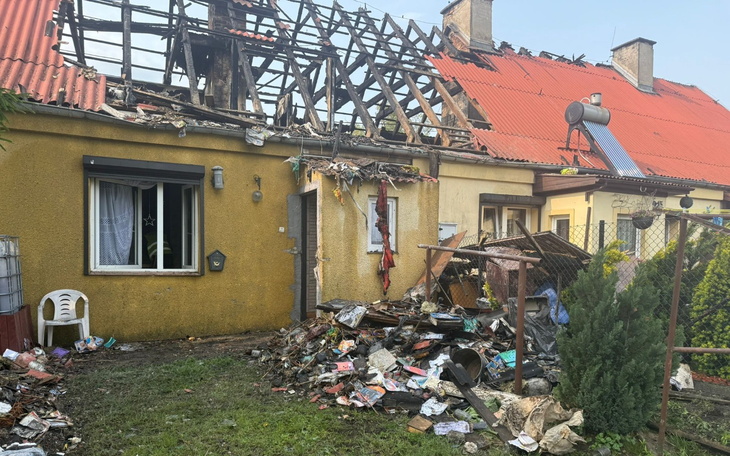 Zniszczony dom po pożarze, z uszkodzonym dachem i bałaganem na podwórku.