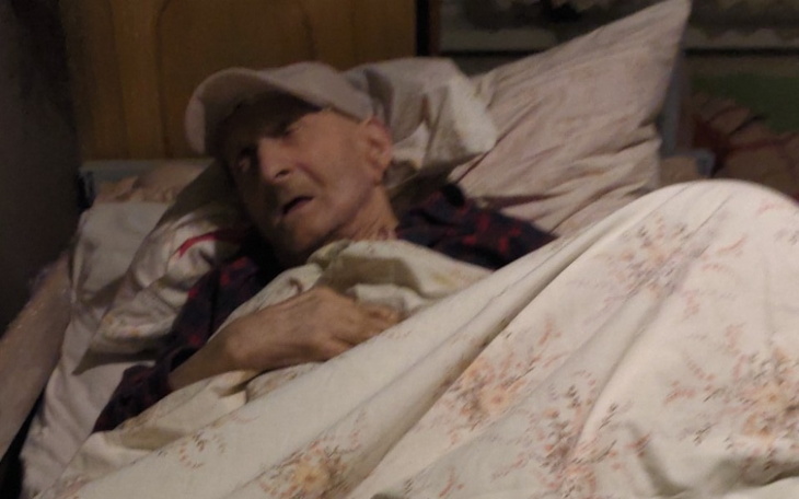 Starszy mężczyzna leżący w łóżku, przykryty kocem.