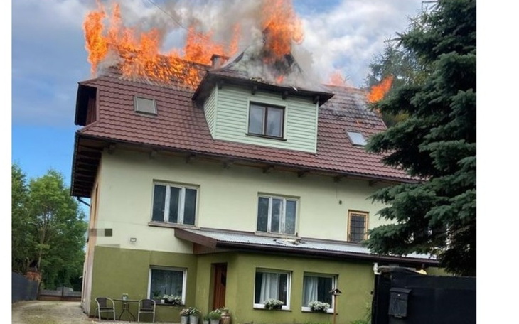 Dom w płomieniach, z dymem unoszącym się z dachu.