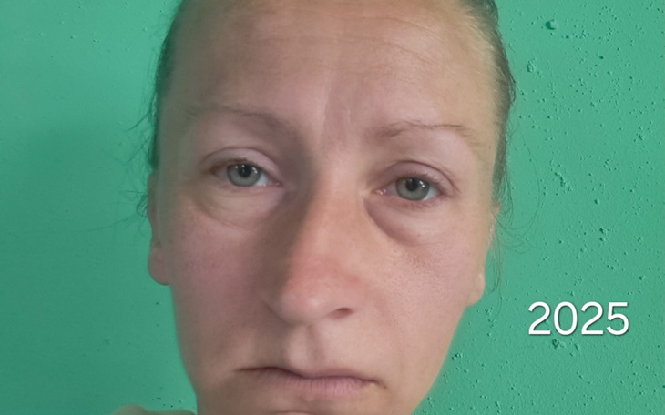 Kobieta z wyrazem smutku na tle zielonej ściany.