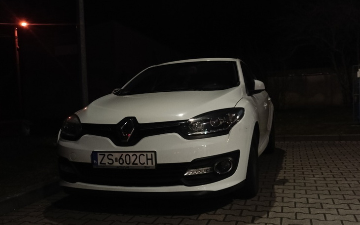 Biały samochód zaparkowany w nocy, oświetlony latarnią.