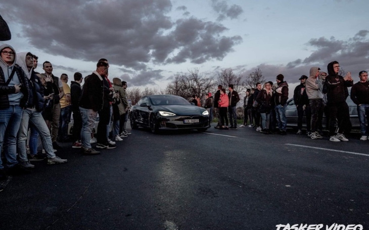 Grupa ludzi zgromadzona wokół samochodu na drodze.