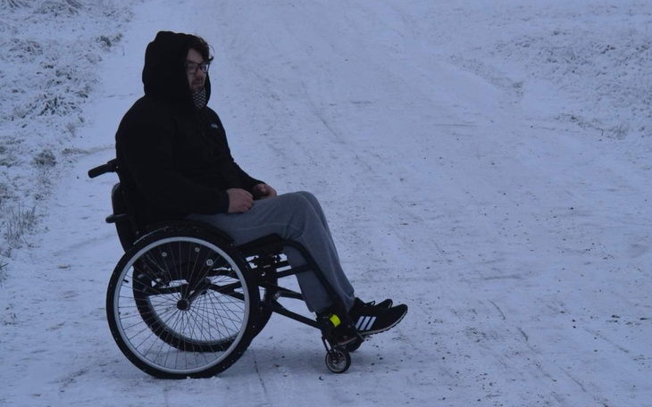 Mężczyzna na wózku inwalidzkim siedzący na zaśnieżonej drodze.