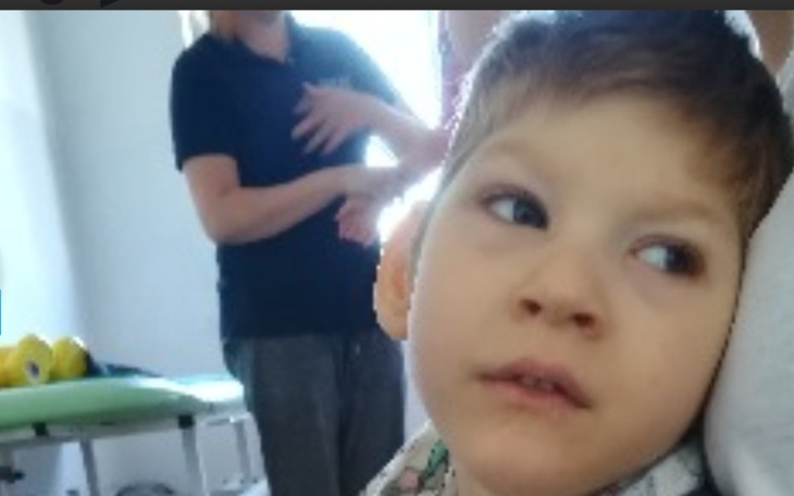 Chłopiec w trakcie terapii, z opiekunem w tle.