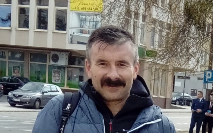 Mężczyzna z wąsami, uśmiechający się na ulicy.