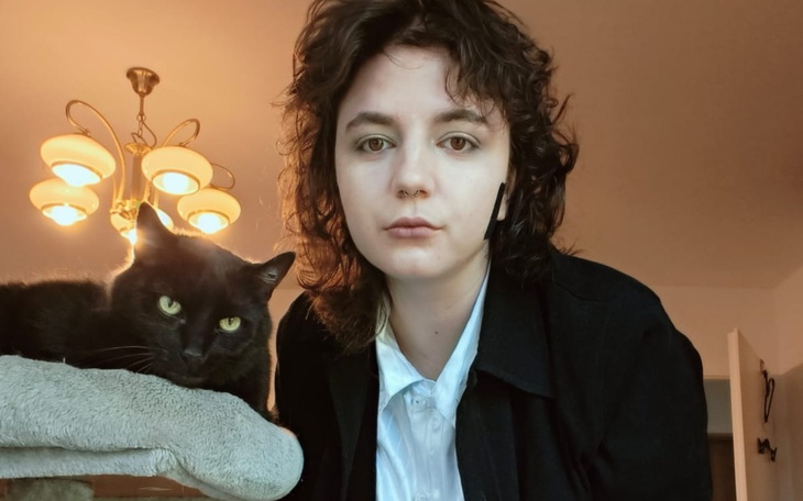 Kobieta z czarnym kotem w tle, w przytulnym wnętrzu.