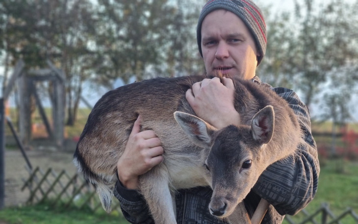 Mężczyzna trzymający sarnę w ramionach, na tle natury.