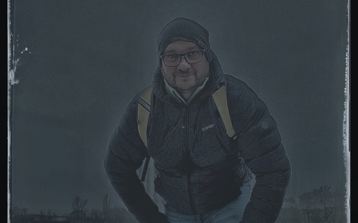 Mężczyzna w ciemnej kurtce, pozujący w deszczowej scenerii.